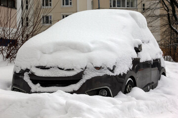 SUV car is covered with snow after a heavy snowfall. Concept of driving in winter time.