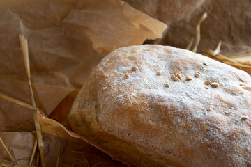 Freshly baked rye bread on a wooden board. Burlap, wheat ,craft paper and straw on the background. Organic bread baked at home from wheat flour.
