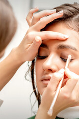 Makeup artist applies eye shadow with a brush on the eye of a beautiful young caucasian woman against a white background