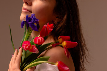 international women's day, a beautiful dark-skinned girl loose her hair and holds spring flowers tulips on her bare shoulder, a little part of the litz is visible, a nude background in the background