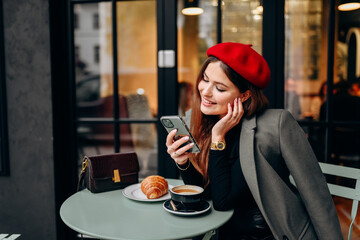 Female blogger chatting with followers in social networks on modern smartphone using 5G internet connection.Hipster girl in watching video on website on cellular in cafe.