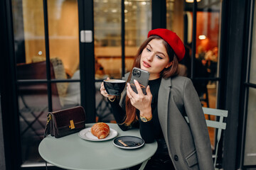 Female blogger chatting with followers in social networks on modern smartphone using 5G internet connection.Hipster girl in watching video on website on cellular in cafe.