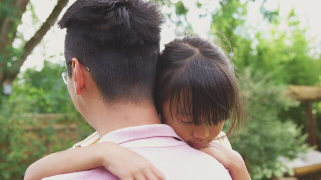 Loving Asian father cuddling daughter in garden as girl looks over his shoulder - shot in slow motion