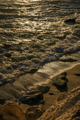 sunset on the shore of the beach with the waves wetting the rocks, stones and the sand