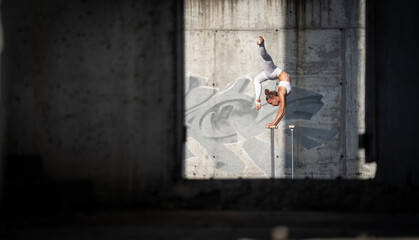 Obraz premium Flexible and fit girl standing on her hands keeping balance in the abandoned building. Concept of motivation, healthy lifestyle and workout 