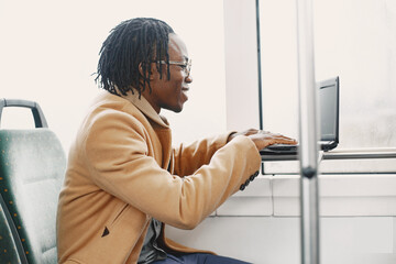 African American man riding in the city bus. Guy in a brown coat. Man with a laptop.