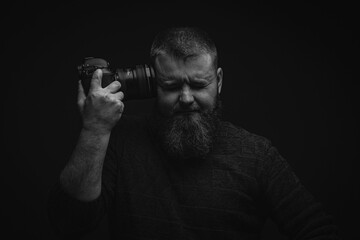 Fototapeta na wymiar Portrait of a man with a beard, who closed his eyes and holds a camera, leaning to his temple, portrait of a man on a black background, soft focus, artistic noise