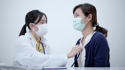 Young doctor wearing protective mask using stethoscope checking heartbeat of female patient.