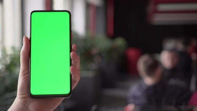 Close up of a woman's hand holding a mobile telephone with a vertical green screen in restaurant chroma key smartphone technology cell phone street touch message display hand