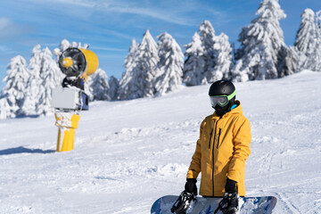 A snowboarder in a yellow jacket poses on the track with a snowboard in his hands.