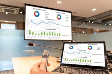 Close up hand holding a remote control slide presentation with presentation meeting on laptop and srceen in meeting room.