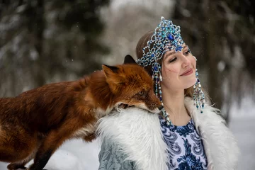 Fotobehang beautiful Russian girl in a winter national dress with a red fox in a winter snowy forest  © константин константи