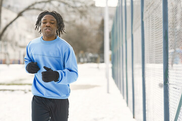 Man in a winter park. African guy training outside. Man run.