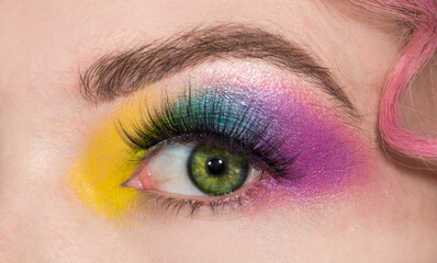 Fototapeta premium Rainbow multicolor stage makeup for the eyes for parties and discos. Open eye with multicolored shadows on the eyelids. Girl with a professional color make-up. LGBT movement flag colors. Stage makeup.