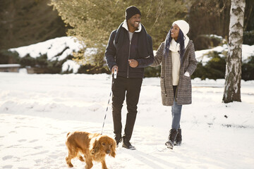 People walks outside. Winter day. African couple with dog.