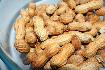 a lot of roasted peanuts in the shell lies in a glass bowl side view