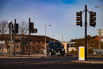 Glasgow, Scotland. Taxi car (London cab) crossing the road and traffic lights. Blue sky background.