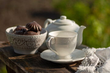 Elegant cup, lace tablecloth, teapot, marshmallow in chocolate, wooden table. Outdoor breakfast,...