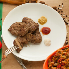 	
Roast meat served with ketchup, mayonnaise, and mustard, sliced piece of meat hanging on a fork. Cooked liver with spices and salad on a white plate standing on the table