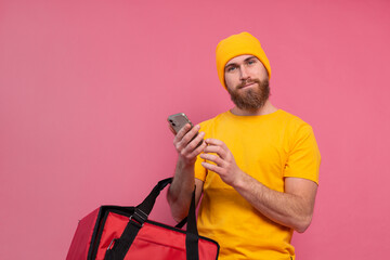 Cheerful european delivery man with bag casual hold phone on pink background