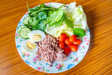A plate of healthy, homemade salad for lunch with tuna, lettuce, boiled egg, tomatoes and sliced cucumber.
