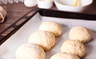 Raw homemade whole grain burger buns on a baking sheet.