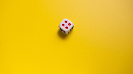 White dice with round dots number four on yellow background close-up. Concept of gambling and chance