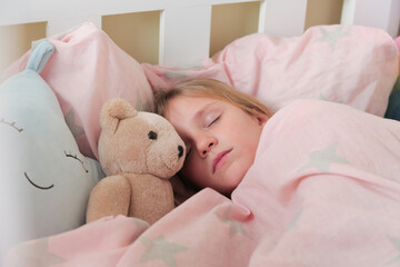 Adorable little girl sleeping with teddy bear in bed .