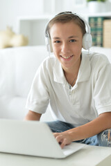 Cute boy in headphones using laptop in room