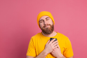 European man got lovely message, holding mobile phone smiling on pink background