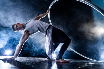 Cyr Wheel circus artist on smoked, dark background performing on stage 