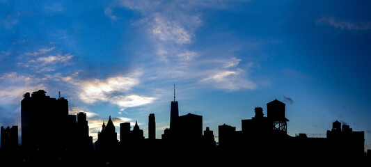Silhouette of the New York City downtown skyline with black buildings contrast against blue sky background