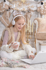 Girl with laptop listening to music near Christmas tree