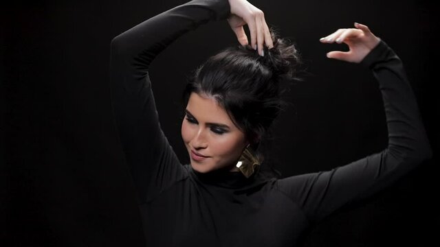 beautiful girl looks at camera and lets her hair down in studio, close up. Curly hair fashion model with dark make-up posing on black background.