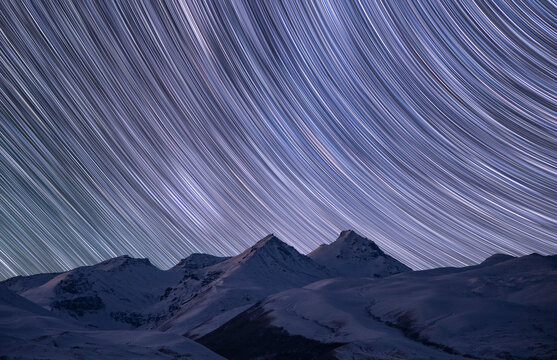 Night winter landscape, the snow-capped mountains under the colorful star trails on the sky. Night time lapse photography.