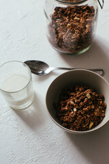 Chocolate granola for breakfast. A jar and and a bowl of muesli and glass of yoghurt