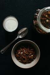 Chocolate granola for breakfast. A jar and and a bowl of muesli and glass of yoghurt