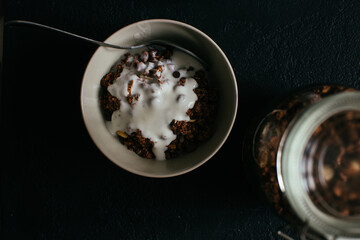 Chocolate granola for breakfast. A jar and and a bowl of muesli and glass of yoghurt