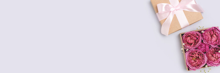 Open gift box with rose flowers inside. Springtime festive composition on a blue pastel background. Banner with copyspace.