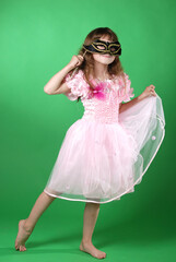 beautiful little girl in pink butterfly dress and carnival mask dancing on green background