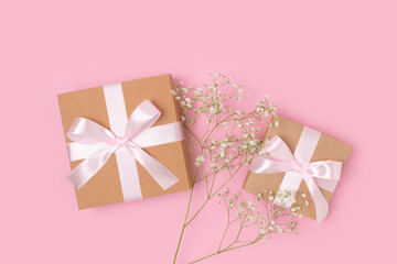 Gift boxes with a tied ribbons and branch of gypsophila flower on a pink background. Congratulation concept with copyspace.
