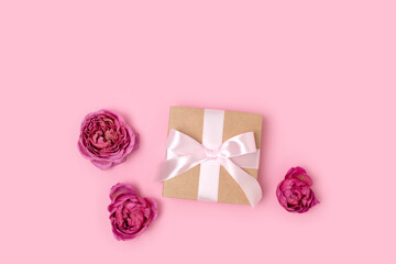 Present with a tied ribbon and heads of rose flower on a pink background. Romantic composition with gift.