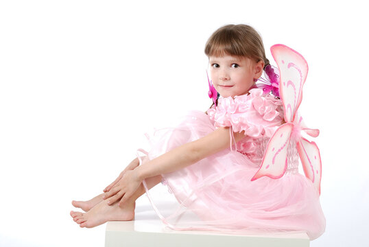 a beautiful little girl in a pink dress with butterfly wings is sitting on a table on a white background.