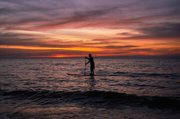 Silhouette man paddling sub board on the sea and colorful sky