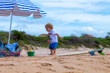 CRIANÇA LOIRA NA PRAIA BRINCANDO COM UMA PRANCHA DE SURF, GUARAPARIA, ES, BRASIL.