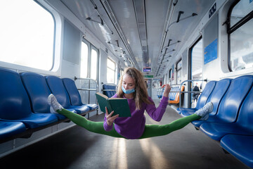 Very flexible wearing mask woman reading book in the subway car sitting in the gymnastic split....