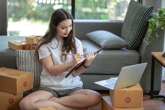 Young Asian Businesswoman Sell Thing Online, Preparing Boxes And Taking Notes For Customer At Home.