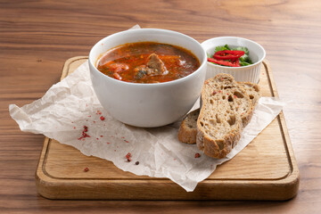 A bowl of Solyanka - a traditional Ukrainian soup made from beets, vegetables and meat with bread on a wooden table.