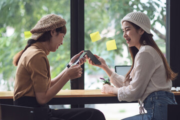 Two young Asian woman playing on mobile phone relaxing at a café.