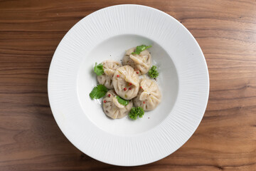 Boiled traditional asian dumplings manti sprinkled with parsley and red pepper in a white plate on a wooden table